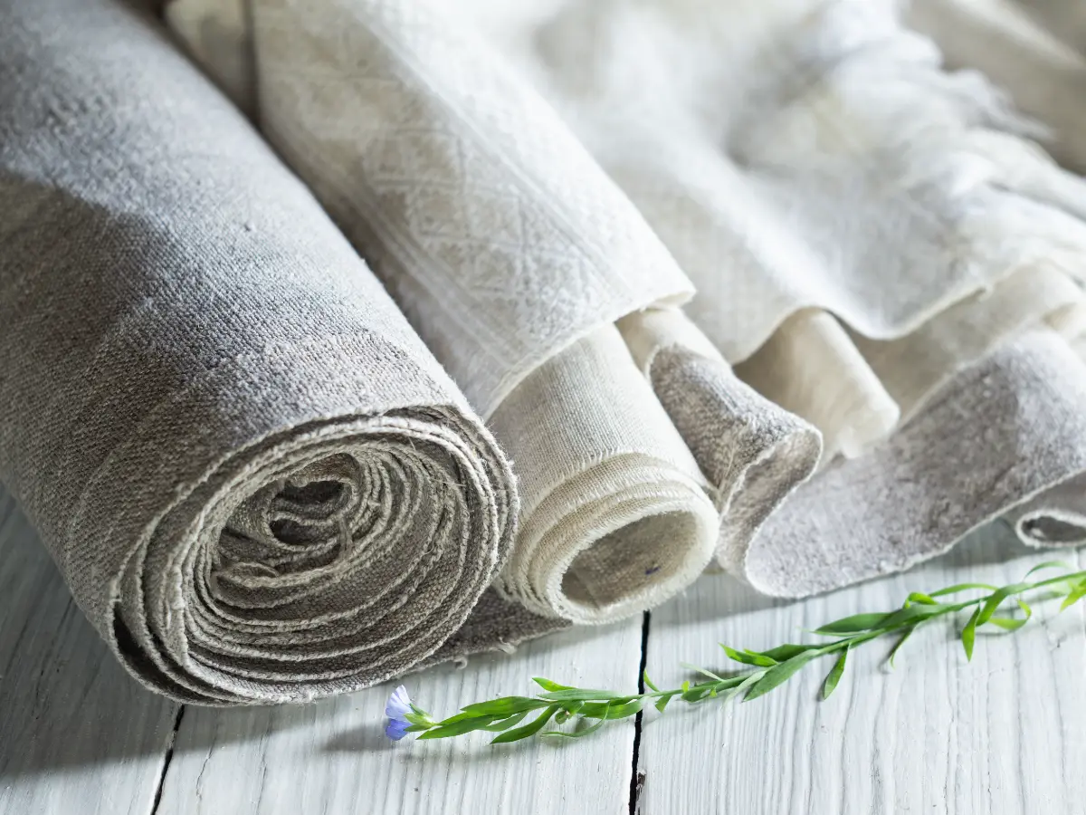 Multiple rolls of fabrics slightly unwound upon a wood table.