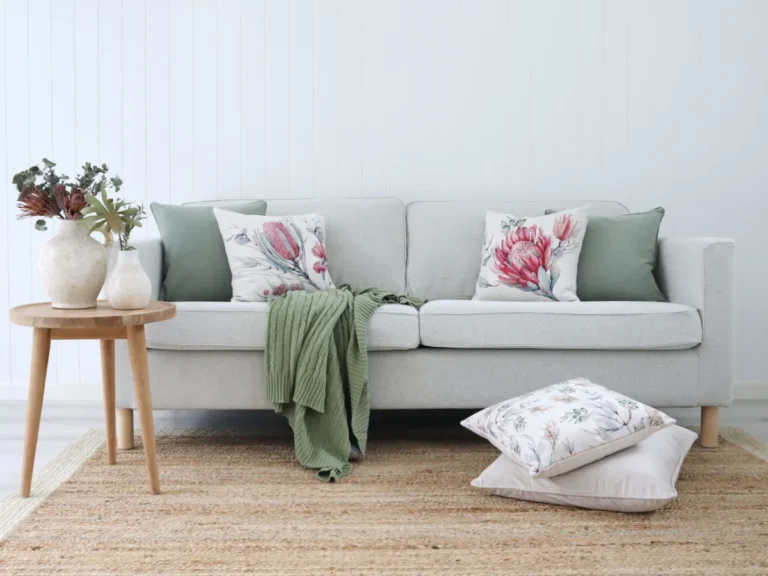 A light coloured room with a sofa that is decorated with floral cushion designs.