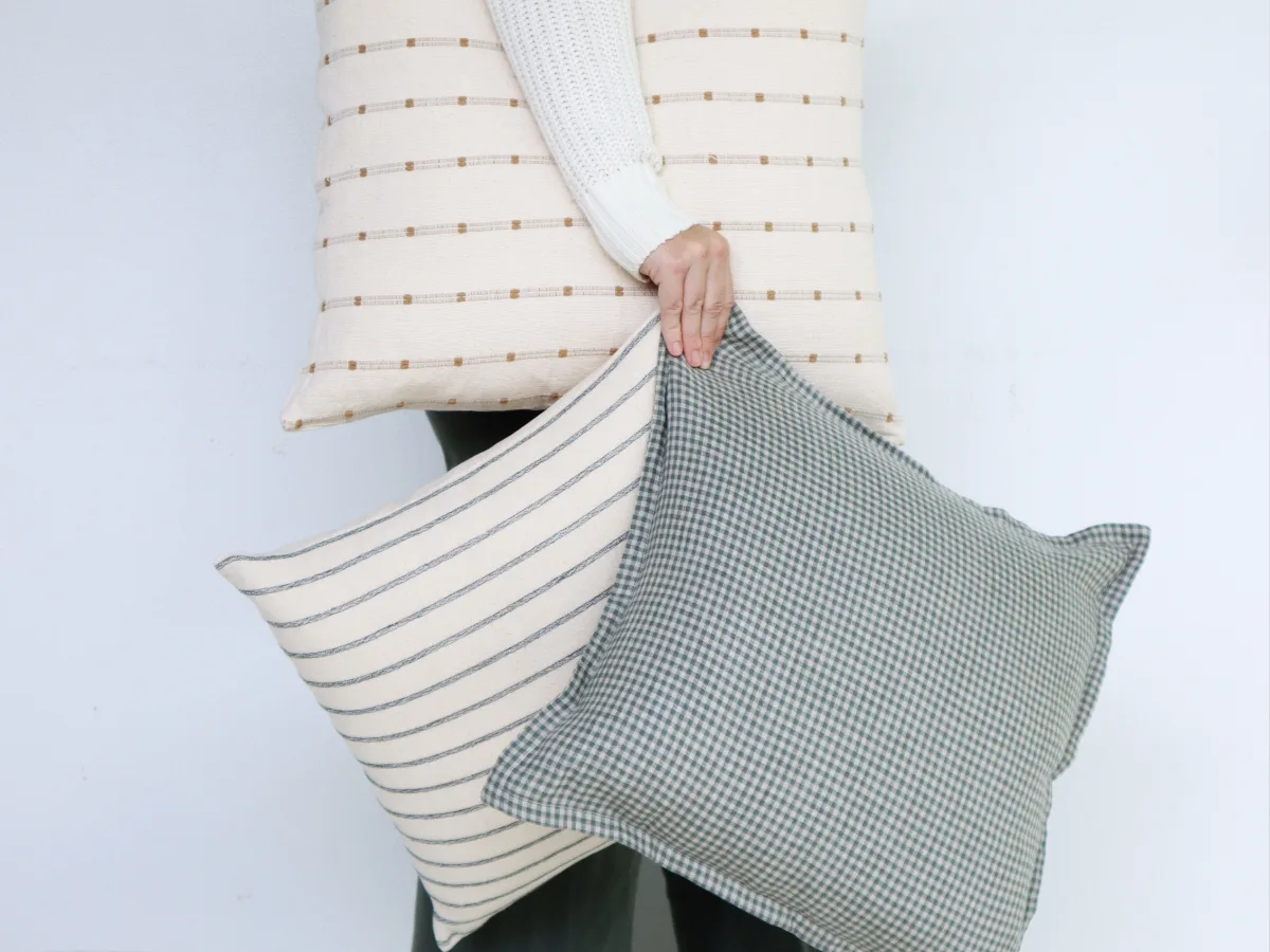 A lady is carrying three cushions in her hand and under her arm.