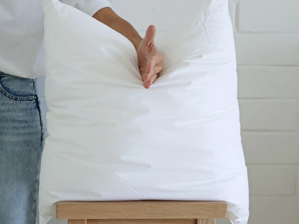 A premium faux feather cushion insert chopped by a stylist's hand whilst on a chair.