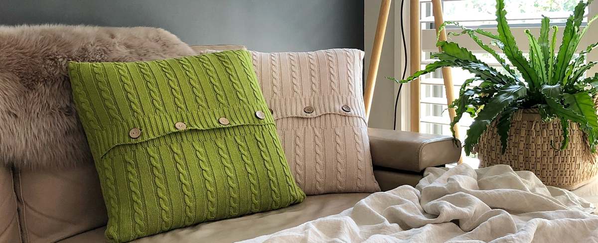 Some wool cushions in green and beige on a sofa.