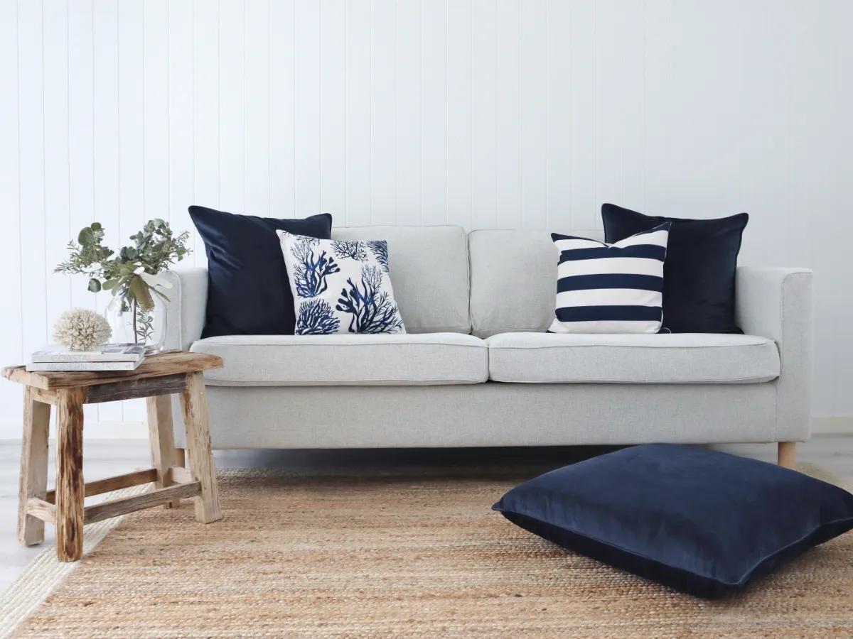 Four navy cushions styled on a 3 seater sofa with a small table nearby.