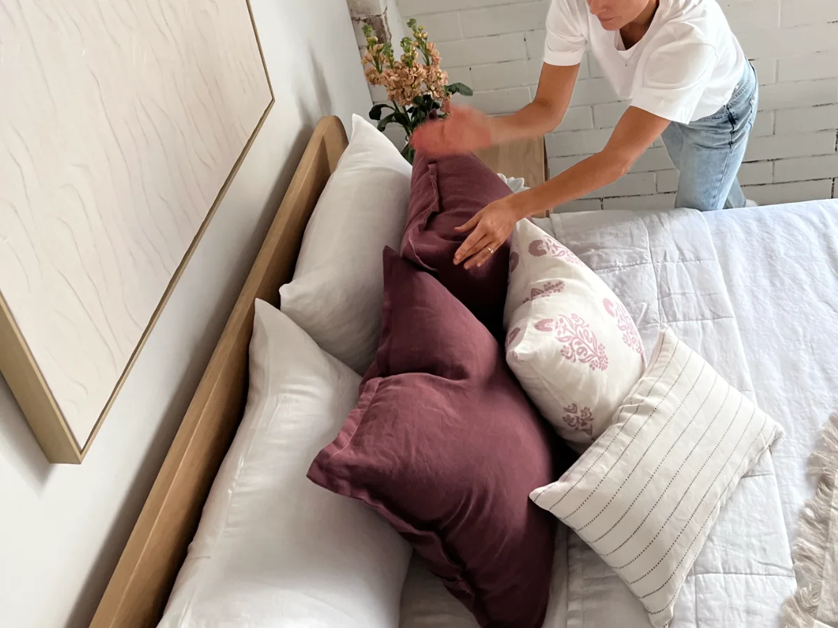 A woman is placing cushions in an arrangement and styling them using the chop method.