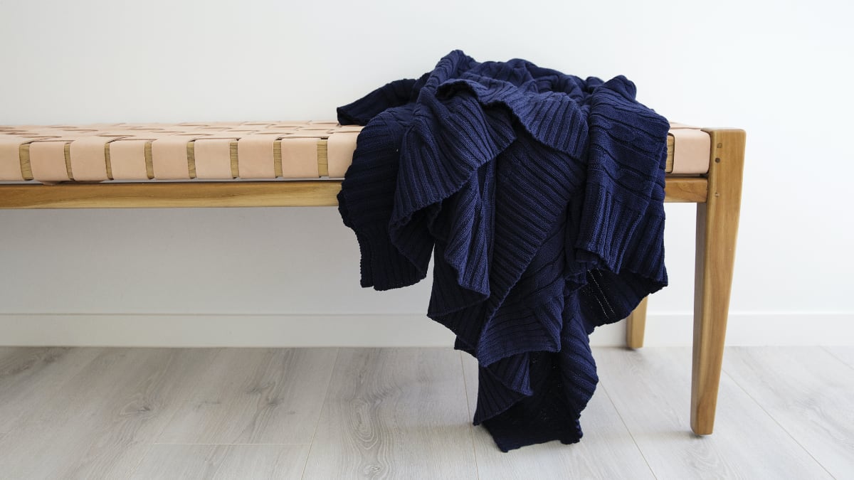 A navy throw rug on a bench that is wooden.