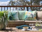 A tropical collection featuring green outdoor cushions lay on an outdoor lounge with a plate of drinks and snacks nearby
