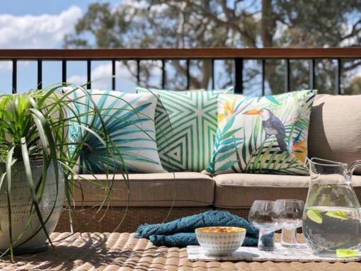 A tropical collection featuring green outdoor cushions lay on an outdoor lounge with a plate of drinks and snacks nearby