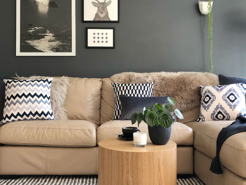 Two grey and white cushions sit within an arrangement on a leather sofa in front of a dark grey wall that features different Scandi influenced artwork