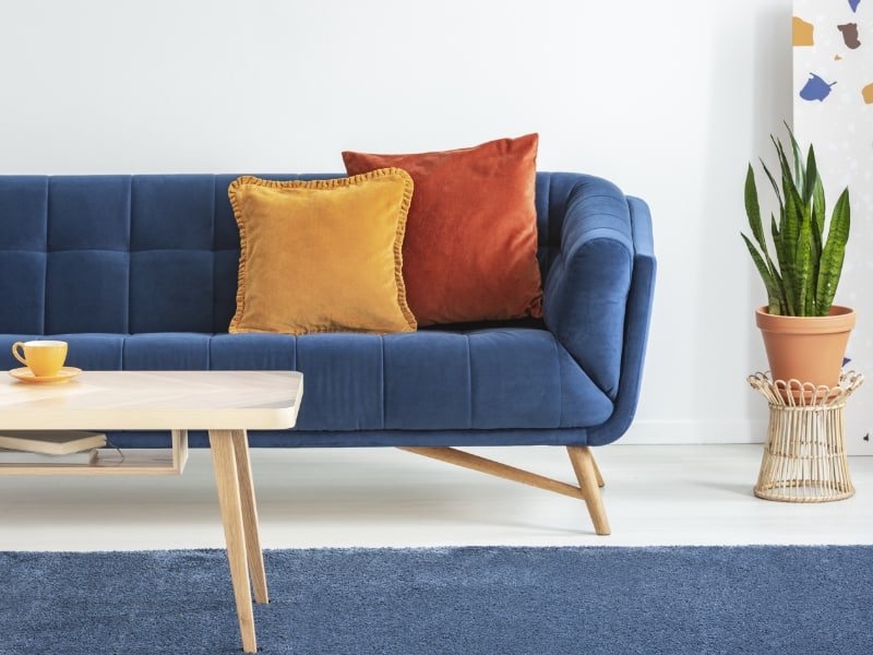 A vibrant living room is shown with a pair of orange cushions displayed on a lovely bright blue sofa with nearby objects like terracotta pots and copper coloured decor adding to the rich vibe