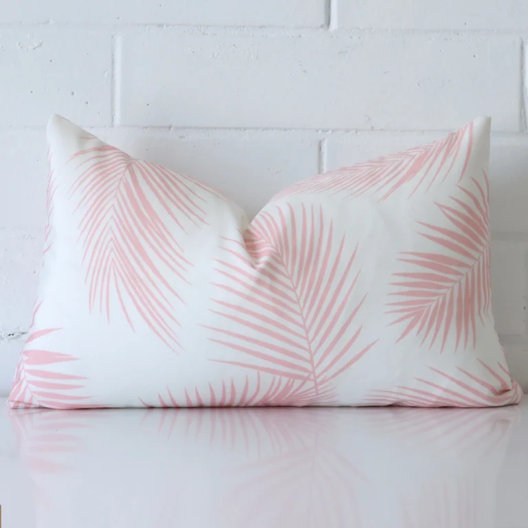 Pink cushion cover in front of a white wall. It has a rectangle size and is made from a outdoor material.