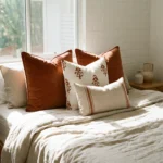 Anna cushions styled on bed with warm rust, patterned and striped neutral cushions.
