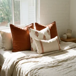 Anna cushions styled on bed with warm rust, patterned and striped neutral cushions.