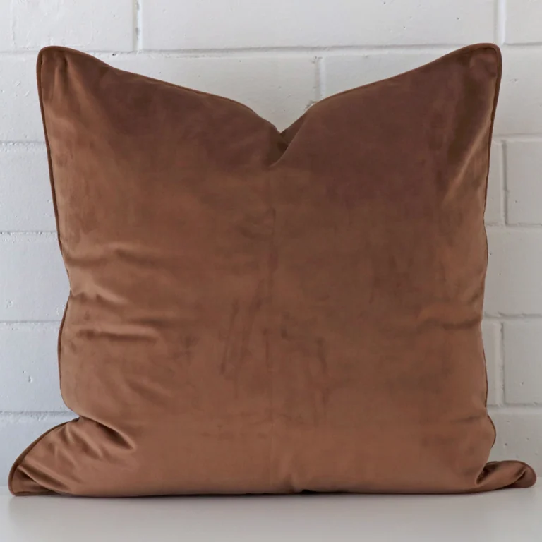 Square cushion cover in brown colour sitting upright in front of a brick wall. It has been made from a quality velvet material.