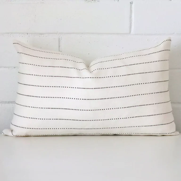 An attractive striped linen cushion in front of a white brick wall. It has a rectangle shape.