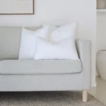 A set of 3 indoor faux feather cushion inserts positioned on the end of a couch.