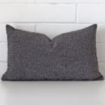 Dark grey cushion cover sits against a white wall. It is constructed from a superior looking boucle material and has rectangle dimensions.