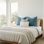 Eva cushions on bed with blue tones, geometric pattern and textured white cushion.