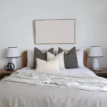 A set of 4 designer bed cushions on a wooden bed between two white lampshades.