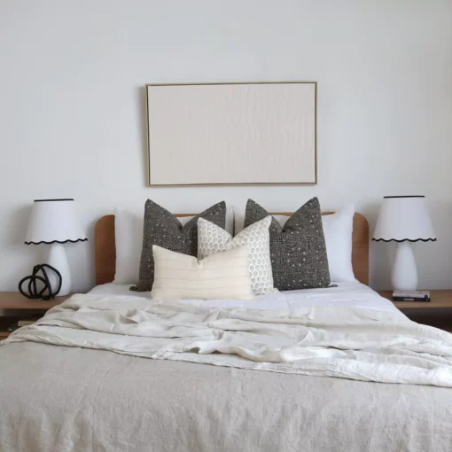 A set of 4 designer bed cushions on a wooden bed between two white lampshades.