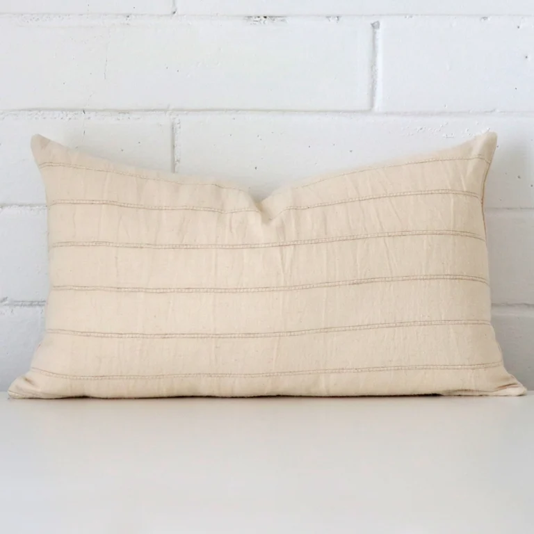 Designer cushion cover features prominently against a white wall. It is a rectangle design and has a striped decorative finish.