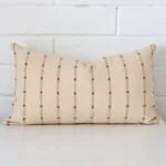 An attractive striped designer cushion in front of a white brick wall. It has a rectangle shape.