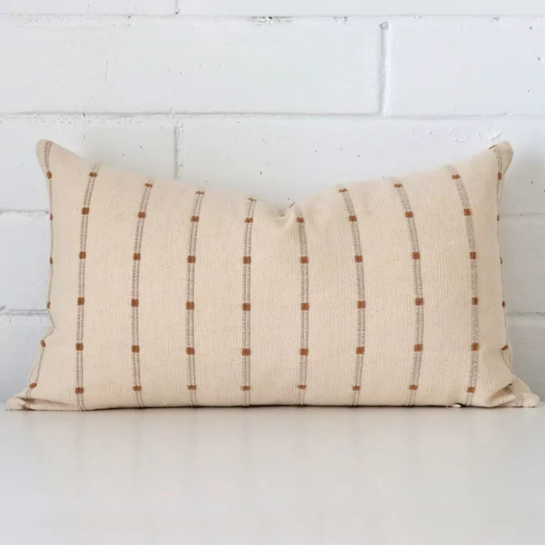 An attractive striped designer cushion in front of a white brick wall. It has a rectangle shape.
