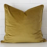 Mustard velvet cushion cover features prominently against a white wall. It is a square design.