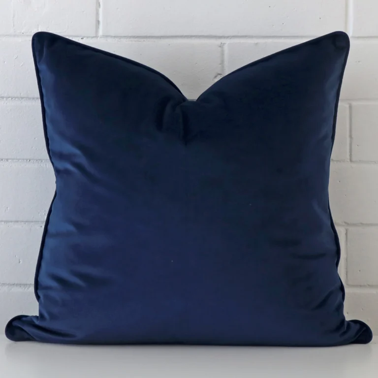 Royal blue Tcushion cover in front of a white wall. It has a large size and is made from a velvet material.