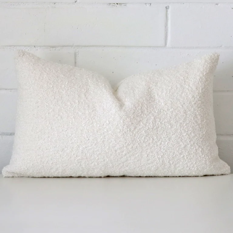 White cushion cover sits against a white wall. It is constructed from a superior looking boucle material and has rectangle dimensions.