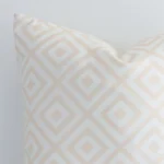 The corner of this beige outdoor cushion is shown close up. The finer detail of its square design and geometric decorative finish can be seen.