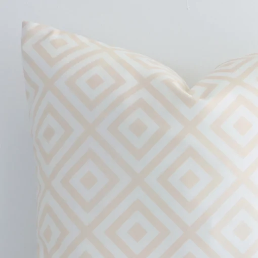 The corner of this beige outdoor cushion is shown close up. The finer detail of its square design and geometric decorative finish can be seen.