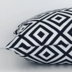 Square black-and-white cushion laid flat. This view shows the geometric style and outdoor fabric from side on.