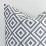 Square geometric cushion in grey colour sitting upright in front of a white wall. It has been made from a quality outdoor material.