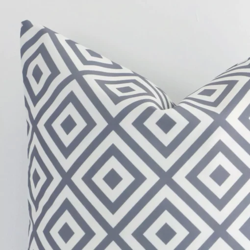 Square geometric cushion in grey colour sitting upright in front of a white wall. It has been made from a quality outdoor material.