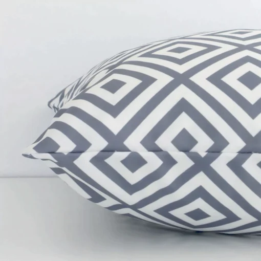 Grey geometric cushion cover laying sideways against white wall. The square size and outdoor material are shown highlighting the seams.