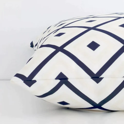 Geometric navy beige cushion laid horizontally. This perspective shows the edge of the outdoor fabric and its square shape.