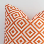 A macro image of the top left corner of this geometric outdoor cushion. It is possible to see the finer detail of the square shape and orange colour.