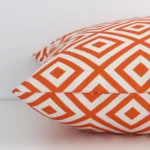 The edge of this outdoor square cushion in orange is shown. The shot shows the geometric design and the front and rear panels.