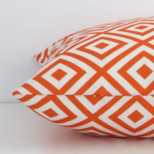 The edge of this outdoor square cushion in orange is shown. The shot shows the geometric design and the front and rear panels.