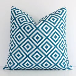 Teal geometric cushion cover in front of a white wall. It has a square size and is made from an outdoor material.