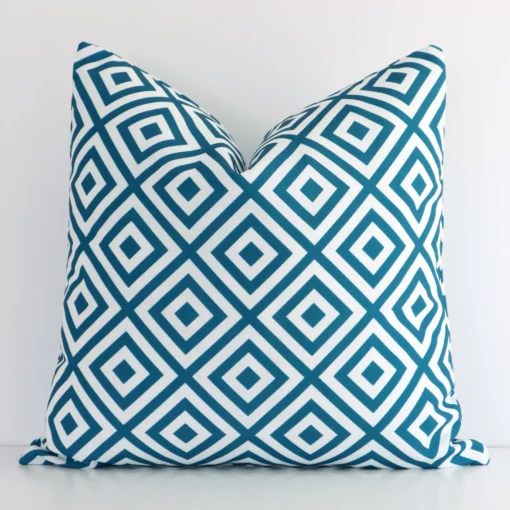 Teal geometric cushion cover in front of a white wall. It has a square size and is made from an outdoor material.