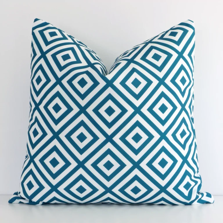 Teal geometric cushion cover in front of a white wall. It has a square size and is made from an outdoor material.