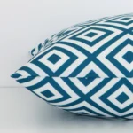 Close side shot of this teal outdoor cushion cover. The viewpoint shows how the square design and outdoor decorative finish meet along its edge.