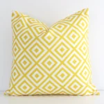 Bold square yellow cushion positioned in front of a white wall. Its geometric style pops on the outdoor fabric.
