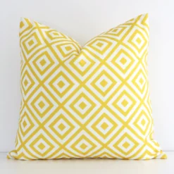 Bold square yellow cushion positioned in front of a white wall. Its geometric style pops on the outdoor fabric.