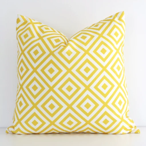 Bold square yellow cushion positioned in front of a white wall. Its geometric style pops on the outdoor fabric.