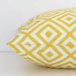 Side angle shot of square cushion cover. The yellow hue and geometric style are shown along its seams.