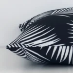 Side perspective showing seam of square black-and-white cushion cover that has a palm motif on its outdoor fabric.