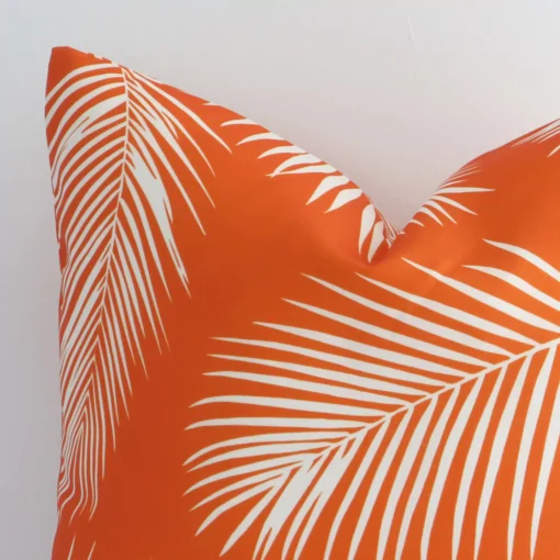 Close up view showing a corner of this palm-designed outdoor cushion in a square size and with orange colouring.