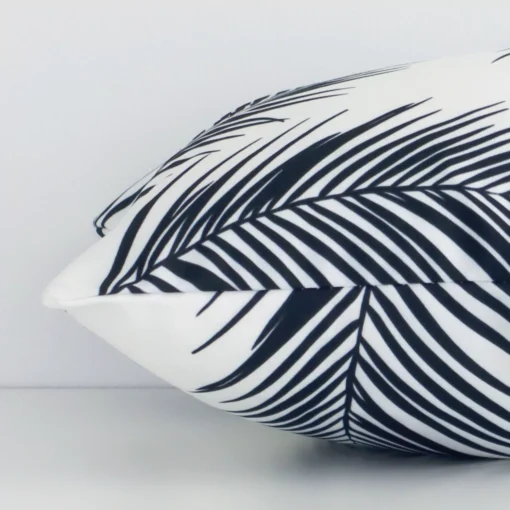 A rectangular outdoor cushion cover positioned flat to showcase the seams. The black-and-white hue and palm tree design are visible between the front and rear fabric panels.
