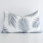Outdoor rectangular cushion with a palm design in an upright position against a white wall. It is grey in colour.